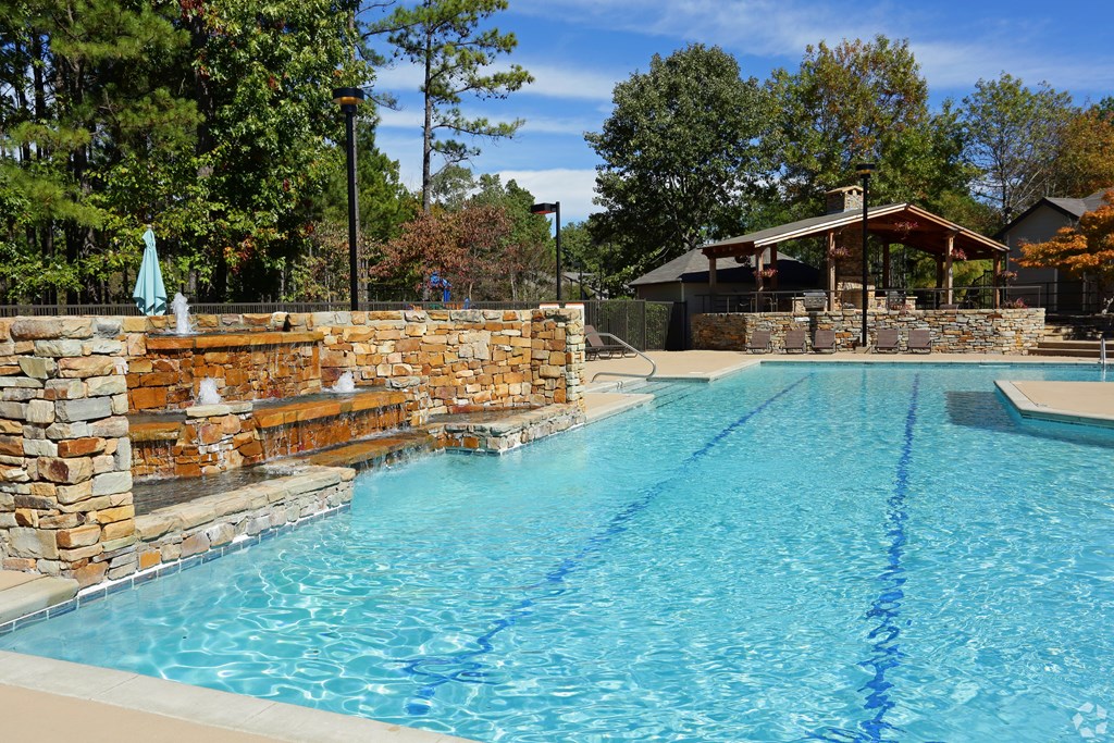 A large swimming pool with a stone wall and a small gazebo in the background.